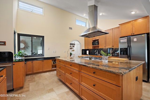 kitchen with a kitchen island, a high ceiling, dark stone counters, appliances with stainless steel finishes, and island exhaust hood