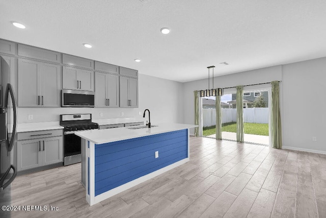 kitchen with pendant lighting, light hardwood / wood-style flooring, a center island with sink, sink, and stainless steel appliances