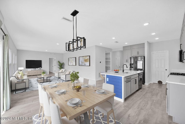 kitchen with gray cabinetry, pendant lighting, a kitchen island with sink, and light hardwood / wood-style flooring