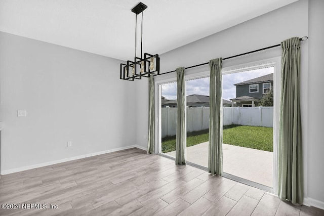 unfurnished dining area with a notable chandelier and light wood-type flooring