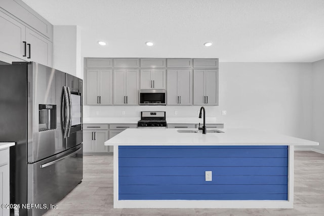 kitchen featuring an island with sink, gray cabinetry, sink, and stainless steel appliances