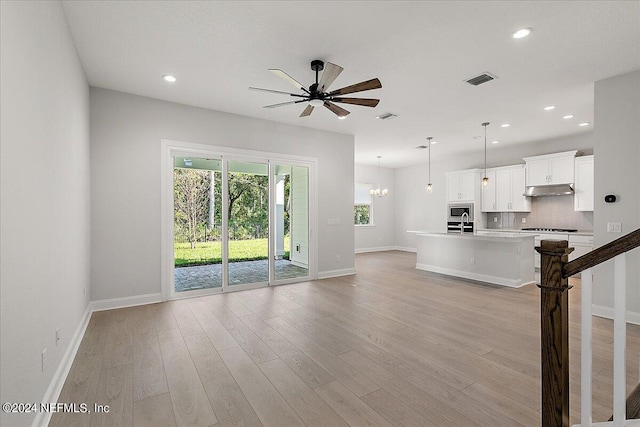 unfurnished living room featuring ceiling fan with notable chandelier and light hardwood / wood-style floors