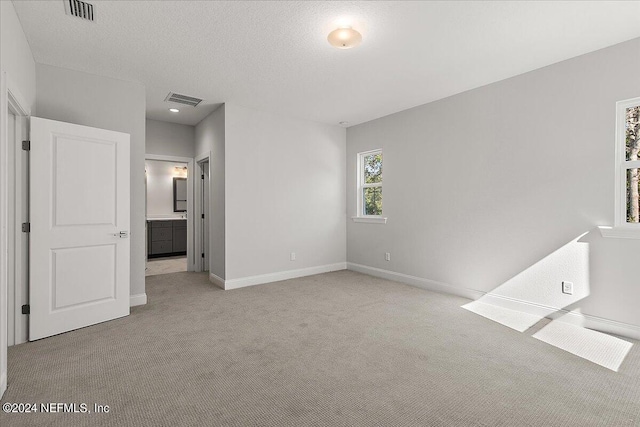 interior space with light colored carpet, a textured ceiling, and ensuite bath