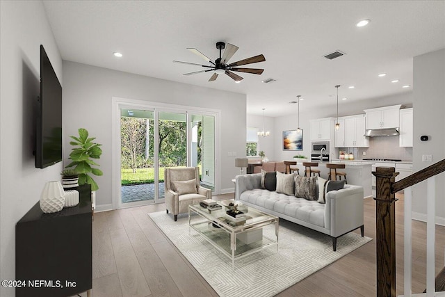 living room with ceiling fan with notable chandelier and light wood-type flooring