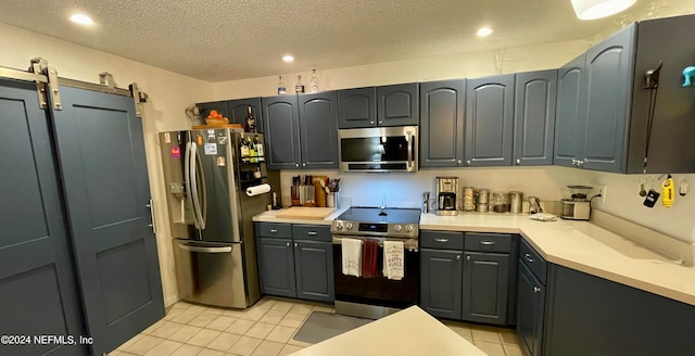 kitchen featuring a barn door, appliances with stainless steel finishes, light tile patterned floors, and a textured ceiling