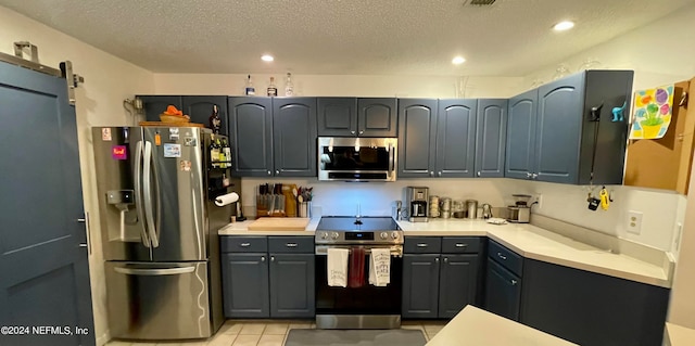 kitchen with light tile patterned floors, a textured ceiling, gray cabinets, stainless steel appliances, and a barn door