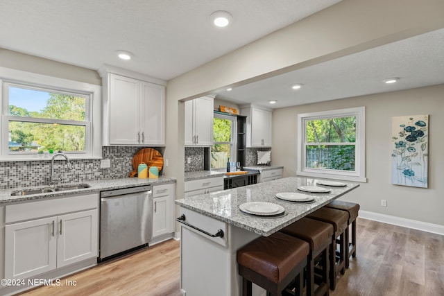 kitchen with white cabinets, light stone counters, a kitchen island, stainless steel dishwasher, and sink