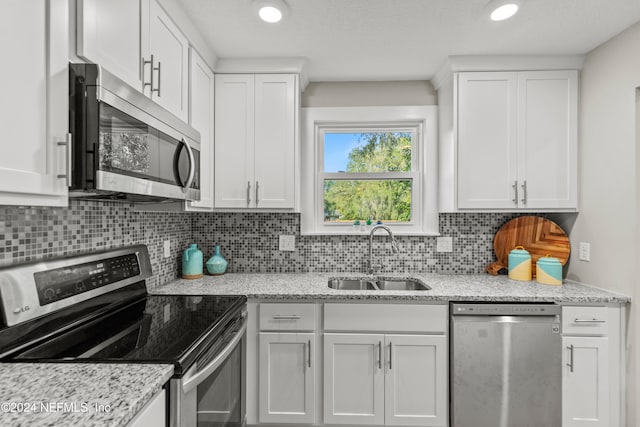 kitchen featuring white cabinets, light stone counters, backsplash, sink, and stainless steel appliances