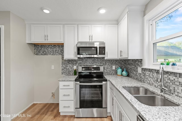 kitchen with stainless steel appliances, sink, white cabinets, light hardwood / wood-style floors, and tasteful backsplash