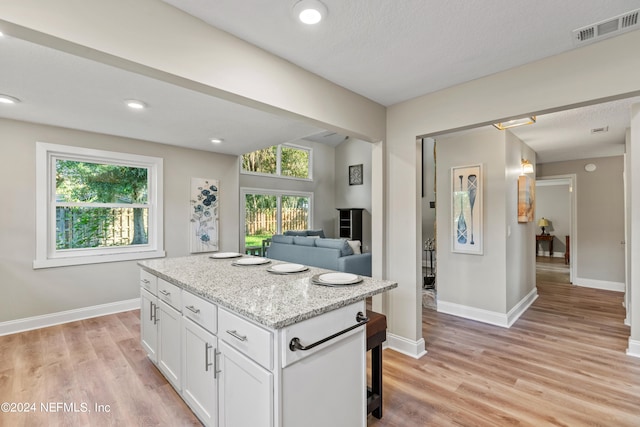 kitchen featuring light stone counters, light hardwood / wood-style flooring, a kitchen island, and white cabinets