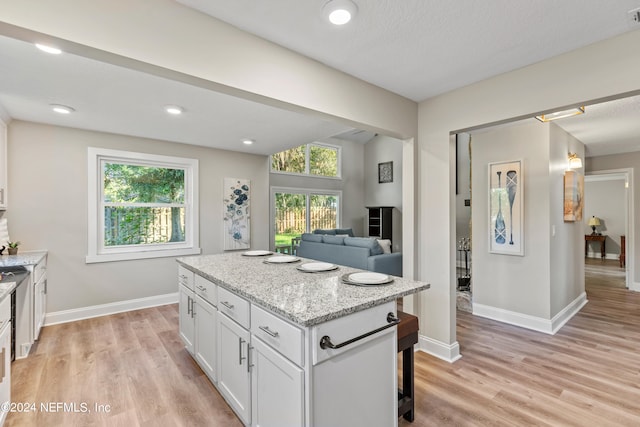 kitchen featuring a center island, white cabinetry, light stone counters, and light hardwood / wood-style floors