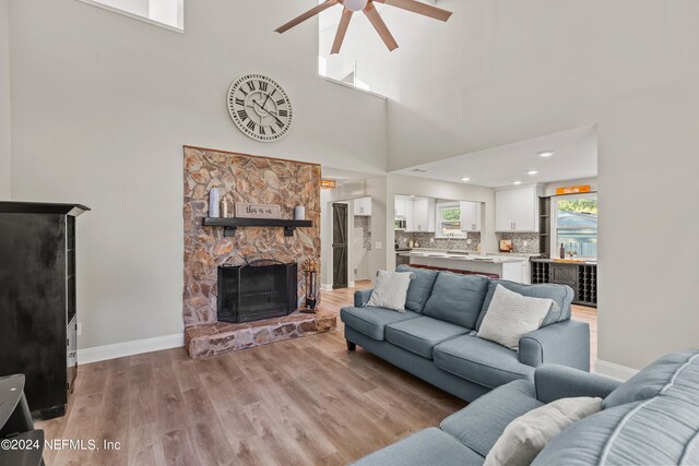 living room with a towering ceiling, light hardwood / wood-style flooring, a stone fireplace, and ceiling fan