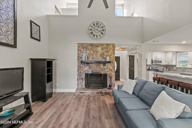 living room featuring a fireplace, a high ceiling, light wood-type flooring, and ceiling fan