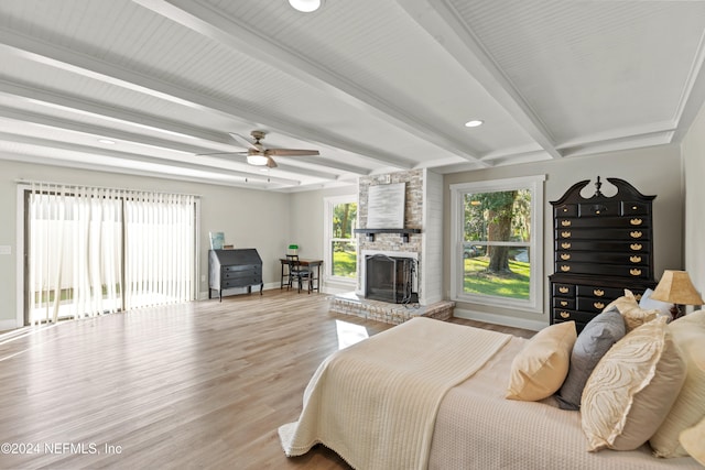 bedroom with beam ceiling, wood-type flooring, a brick fireplace, and ceiling fan