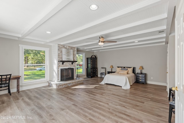 bedroom featuring ceiling fan, beamed ceiling, light hardwood / wood-style flooring, and a fireplace