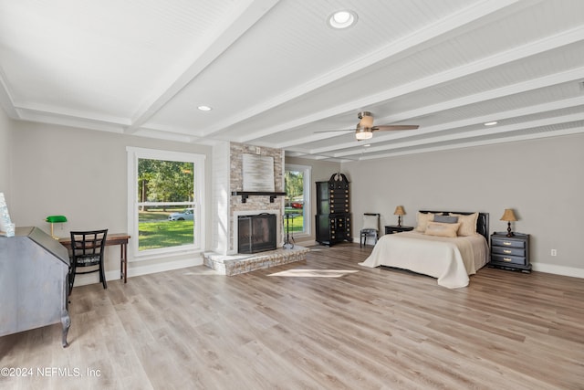 bedroom with light hardwood / wood-style floors, beam ceiling, a large fireplace, and ceiling fan