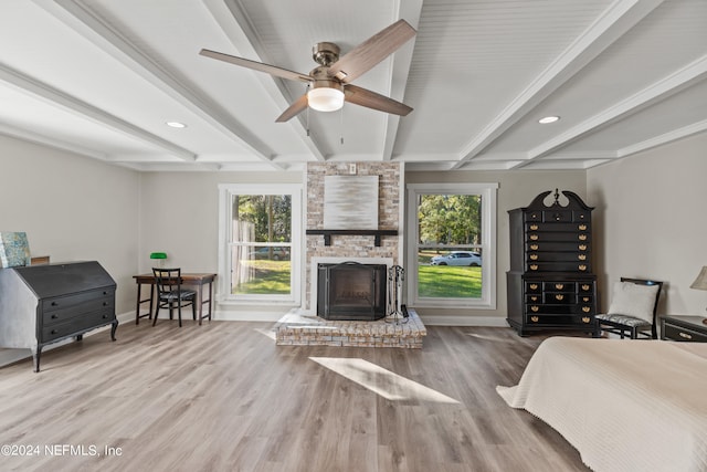 bedroom featuring hardwood / wood-style floors, beamed ceiling, a large fireplace, and ceiling fan