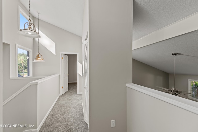 corridor featuring a textured ceiling, high vaulted ceiling, and carpet flooring