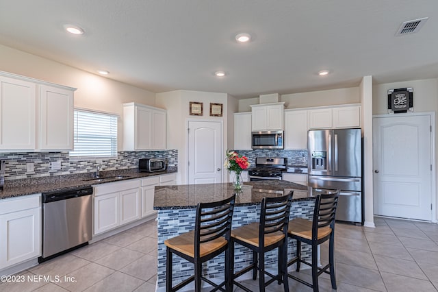 kitchen featuring white cabinetry, appliances with stainless steel finishes, a center island, dark stone countertops, and a kitchen bar