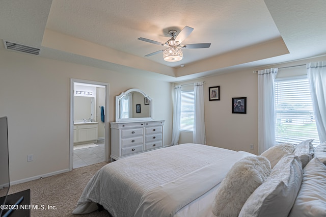 carpeted bedroom featuring ceiling fan, a textured ceiling, a tray ceiling, and ensuite bath