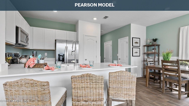 kitchen featuring kitchen peninsula, appliances with stainless steel finishes, a breakfast bar, light hardwood / wood-style flooring, and white cabinetry