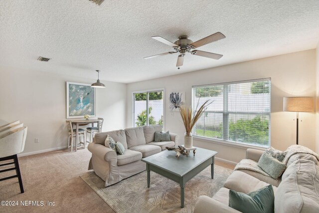 living room with a textured ceiling, ceiling fan, and light colored carpet