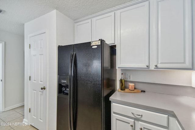 kitchen featuring light tile patterned flooring, black fridge, a textured ceiling, and white cabinetry