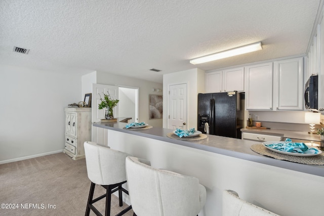 kitchen featuring a textured ceiling, black fridge with ice dispenser, white cabinetry, light colored carpet, and a breakfast bar area