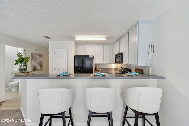 kitchen with a breakfast bar area, kitchen peninsula, white cabinets, black appliances, and a textured ceiling