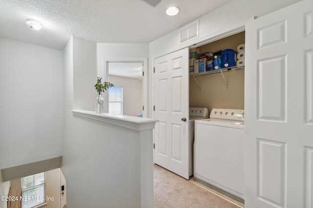 laundry area with washer and clothes dryer, light colored carpet, and a textured ceiling