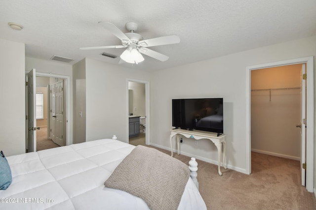 bedroom with ceiling fan, a closet, a spacious closet, light colored carpet, and ensuite bathroom