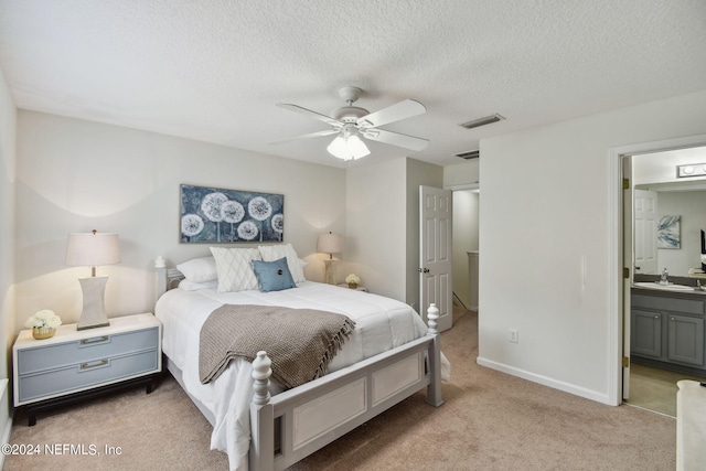 bedroom with ceiling fan, sink, connected bathroom, light colored carpet, and a textured ceiling