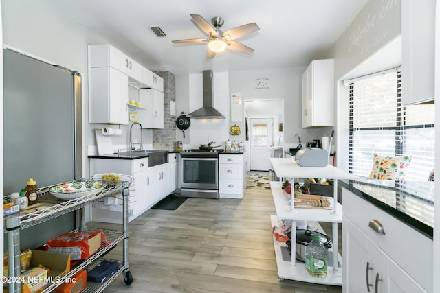 kitchen featuring wall chimney range hood, white cabinets, stainless steel electric stove, and light hardwood / wood-style flooring