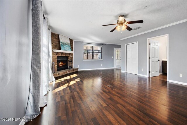 unfurnished living room featuring a textured ceiling, a brick fireplace, ceiling fan, dark wood-type flooring, and crown molding