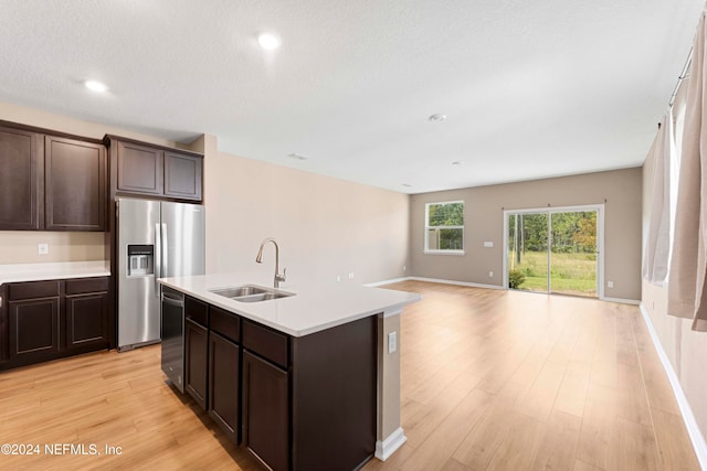 kitchen featuring light wood-type flooring, dark brown cabinets, a center island with sink, sink, and appliances with stainless steel finishes