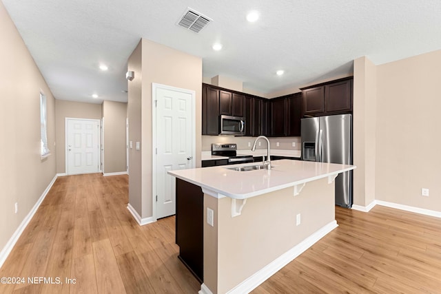 kitchen with dark brown cabinetry, a textured ceiling, a kitchen island with sink, light hardwood / wood-style flooring, and stainless steel appliances