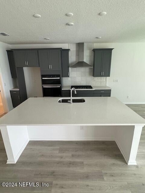 kitchen with wall chimney exhaust hood, wood-type flooring, a center island with sink, and sink