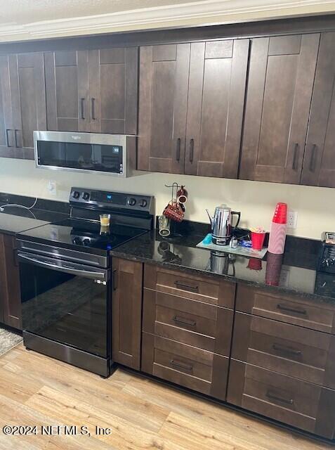 kitchen featuring dark brown cabinets, dark stone countertops, light hardwood / wood-style flooring, and range with electric cooktop