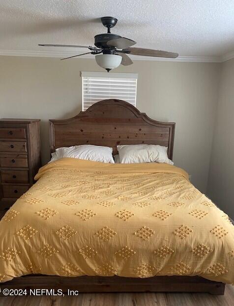 bedroom with wood-type flooring, ornamental molding, a textured ceiling, and ceiling fan