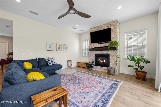 living room featuring light wood-type flooring, ceiling fan, and a stone fireplace