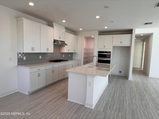 kitchen featuring sink, a kitchen island with sink, backsplash, black appliances, and white cabinets