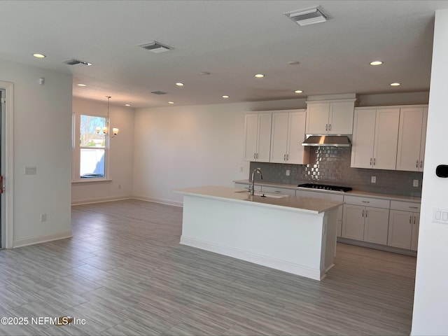 kitchen with sink, white cabinets, black gas stovetop, a center island with sink, and an inviting chandelier