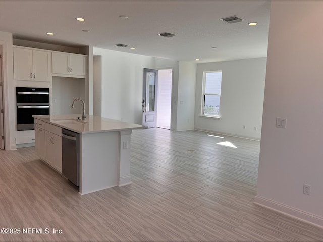 kitchen with sink, multiple ovens, dishwasher, white cabinets, and a kitchen island with sink