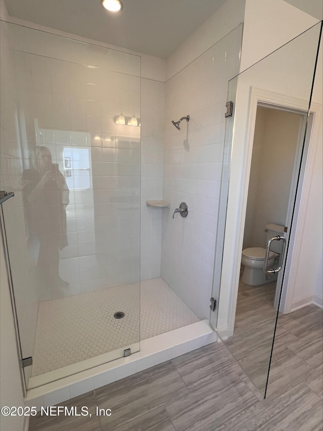 bathroom featuring a shower with door and toilet