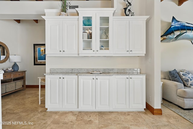 kitchen featuring glass insert cabinets, baseboards, light stone countertops, and white cabinetry