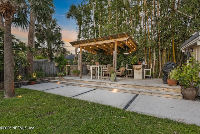 patio terrace at dusk with a lawn, a deck, and fence