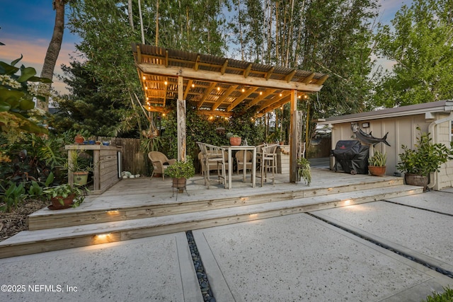 patio terrace at dusk with area for grilling, outdoor dining area, a deck, fence, and a pergola
