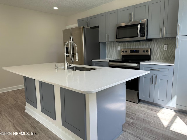 kitchen with tasteful backsplash, a center island with sink, appliances with stainless steel finishes, and light hardwood / wood-style flooring