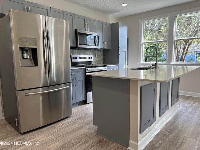 kitchen with a kitchen island with sink, stainless steel appliances, sink, light hardwood / wood-style floors, and a textured ceiling