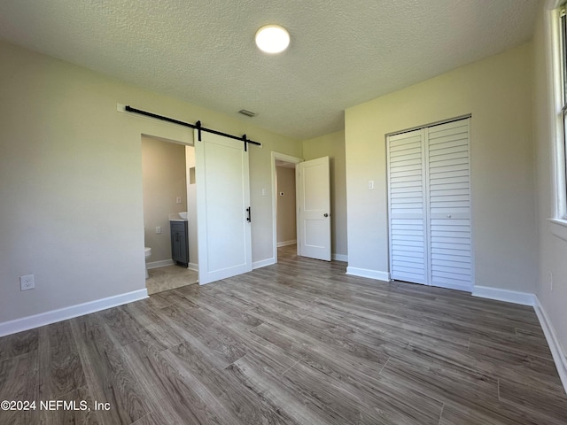 unfurnished bedroom with a closet, hardwood / wood-style flooring, ensuite bath, a barn door, and a textured ceiling